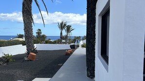 A pathway leading to a building with a view of the ocean and palm trees. - Villa Blanca 2, FKK - Lanzarote, Charco del Palo, Schönes Schwimmbad (Charco del Palo)