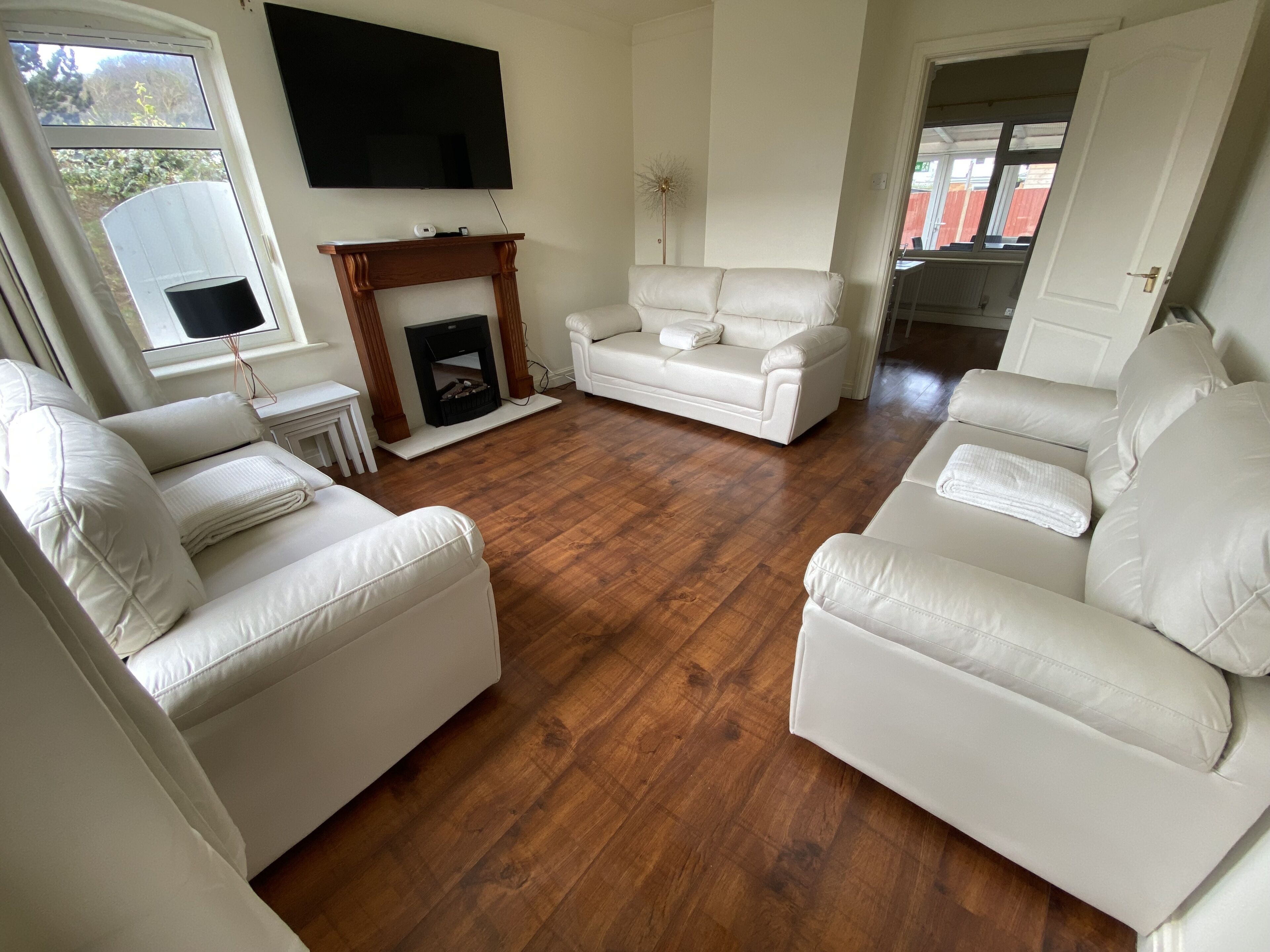 Ein Wohnzimmer mit Kamin, weißen Ledersofas, einem Flachbildfernseher und Holzboden.