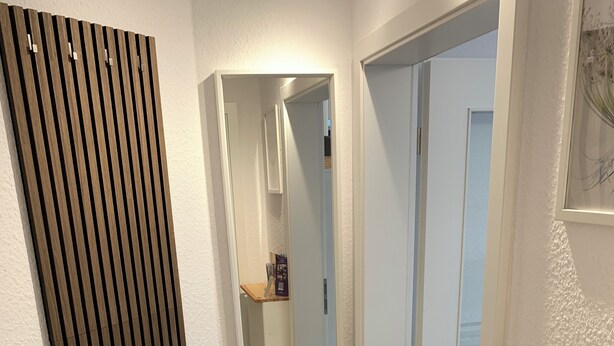 A hallway with a wooden slat wall, a mirror, and a wooden counter with brochures. - Modernes Zentrumsnahes Apartment (Oldenburg)