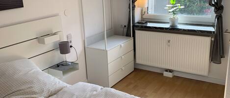 A bedroom with a bed, a dresser, a radiator, and a window with curtains.