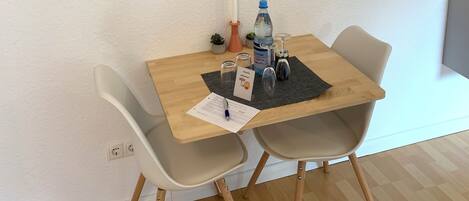 Un comedor con una mesa de madera, dos sillas, una obra de arte enmarcada, una vela, una botella de agua y un menú.