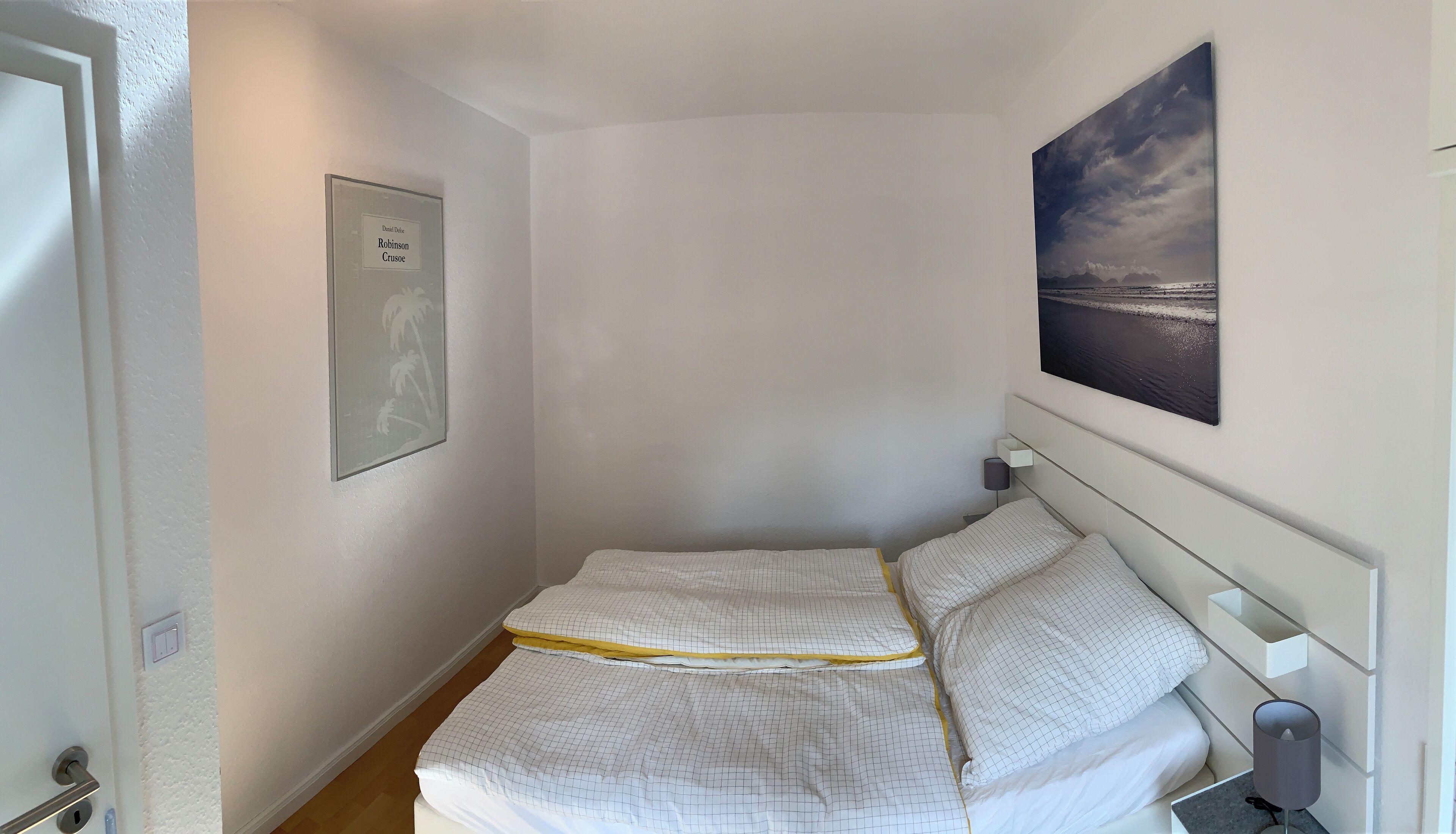 A bedroom with a bed, a nightstand, a lamp, a framed picture, and a painting on the wall.