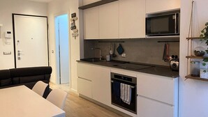 Cocina moderna con microondas, horno y lavavajillas. Cuenta con un comedor con mesa y sillas blancas.