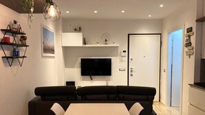 Una sala de estar moderna con un conjunto de sofá, un televisor de pantalla plana montado en la pared y una mesa de comedor con sillas.