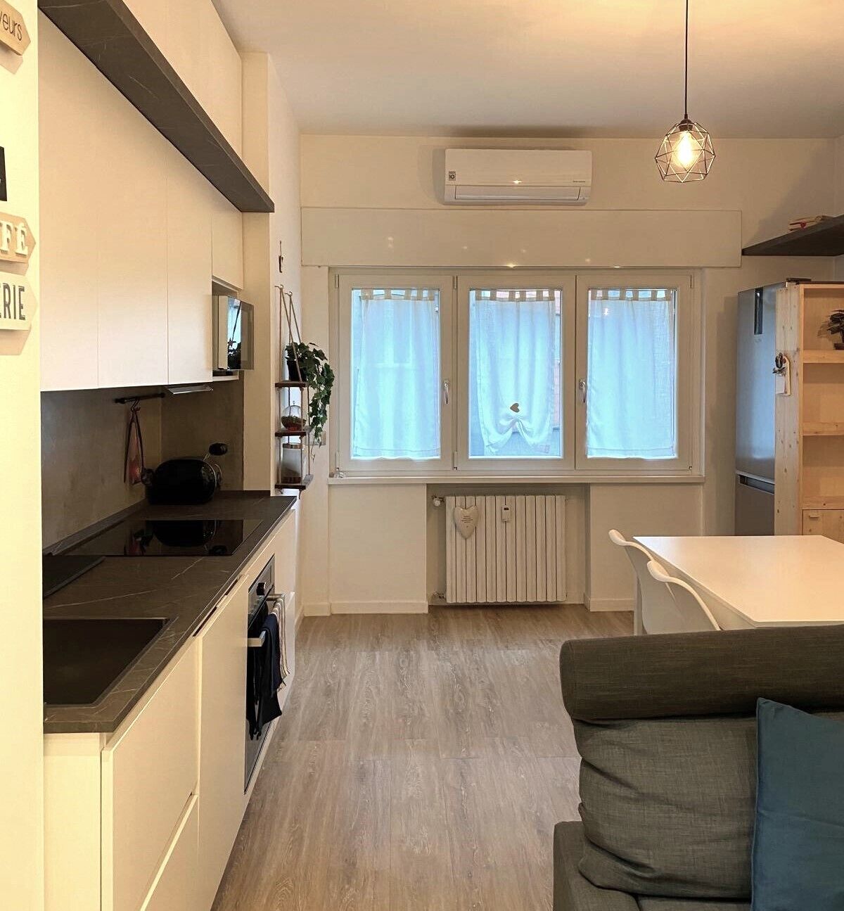 Una cucina moderna con mobili bianchi, un piano di lavoro nero e una finestra con tende.