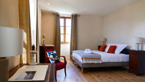 Ein Hotelzimmer mit einem Bett, einem Sessel, einem Schreibtisch mit Lampe und einem fensterbepflanzten Fenster.