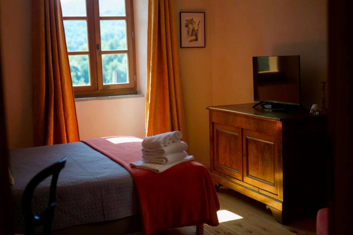 A bedroom with a bed, a television on a wooden cabinet, and a window with curtains.