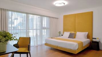A hotel room with a bed, a chair, a table, and a window with curtains.