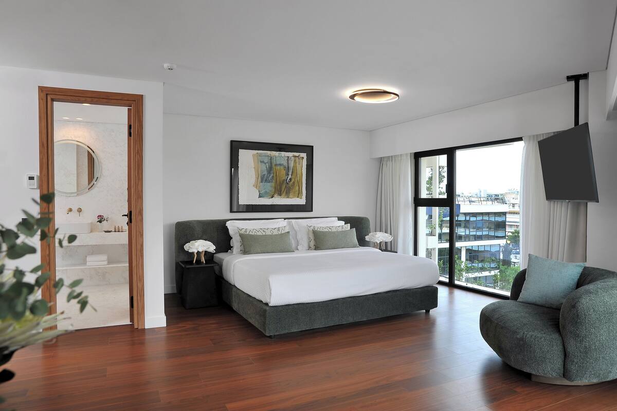A modern bedroom with a large bed, a view of the city, and a balcony.