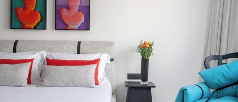 Un dormitorio ordenado con una cama, almohadas, una mesita de noche con un jarrón y una silla.