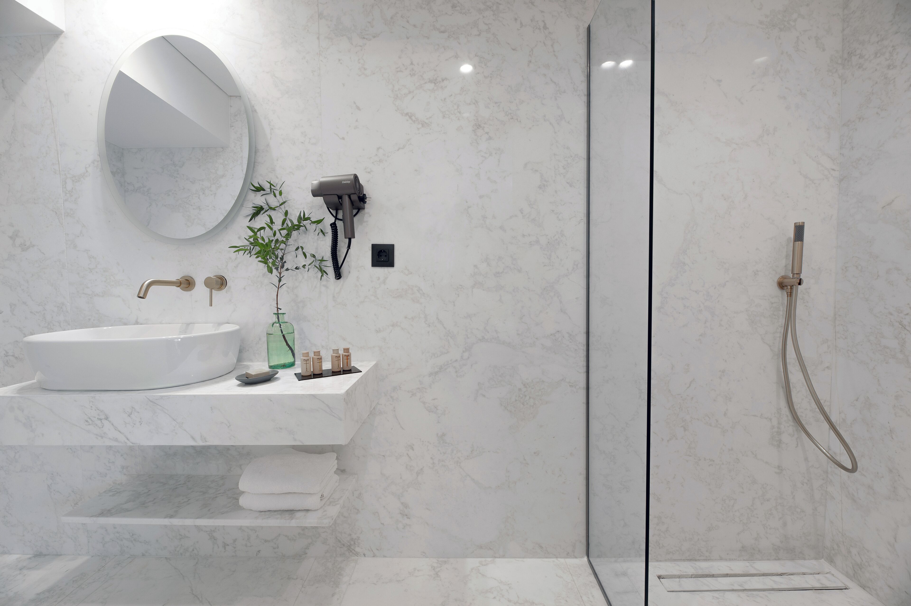 A modern bathroom with a round mirror, a white sink, and a handheld showerhead.
