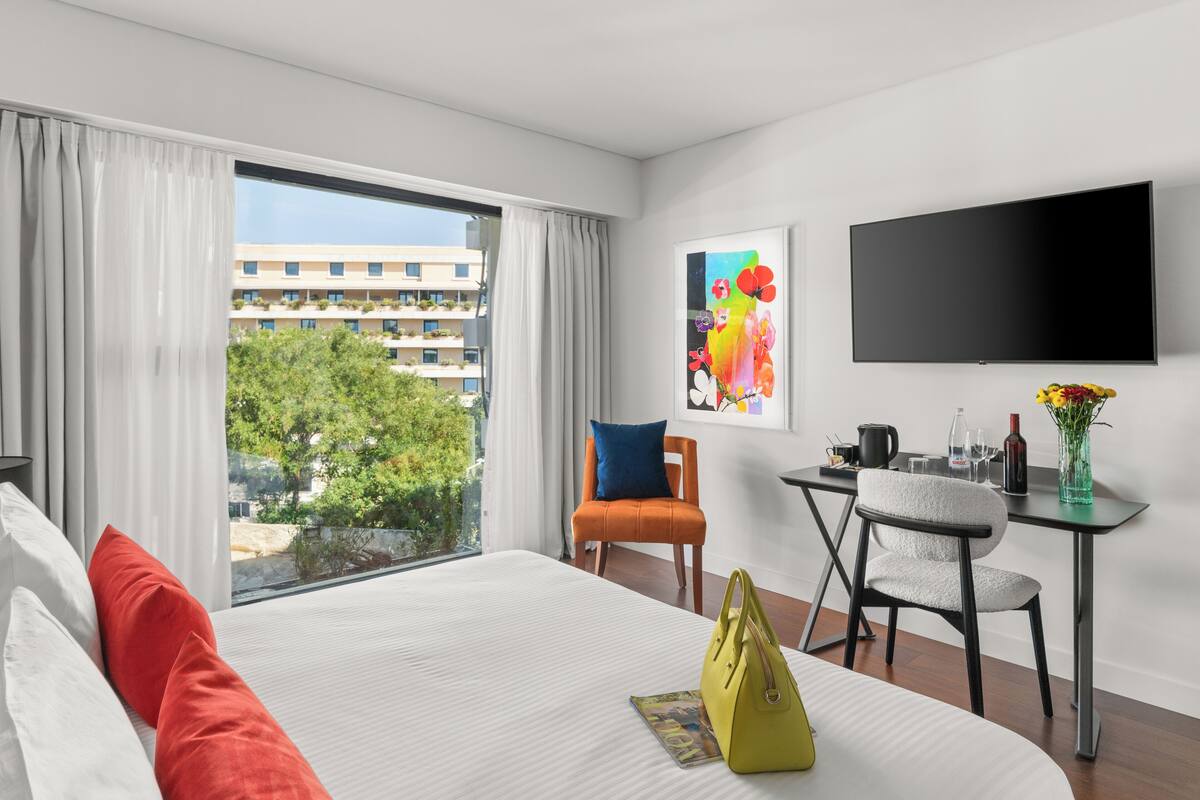 A hotel room with a large bed, a desk with a chair, a TV, and a window with curtains.