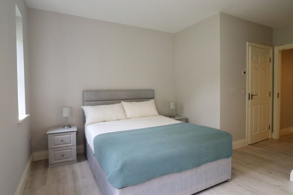 A bedroom with a bed, nightstands, a door, and a window. - Inviting 2-bed Apartment in Dublin (Ballyboghil)