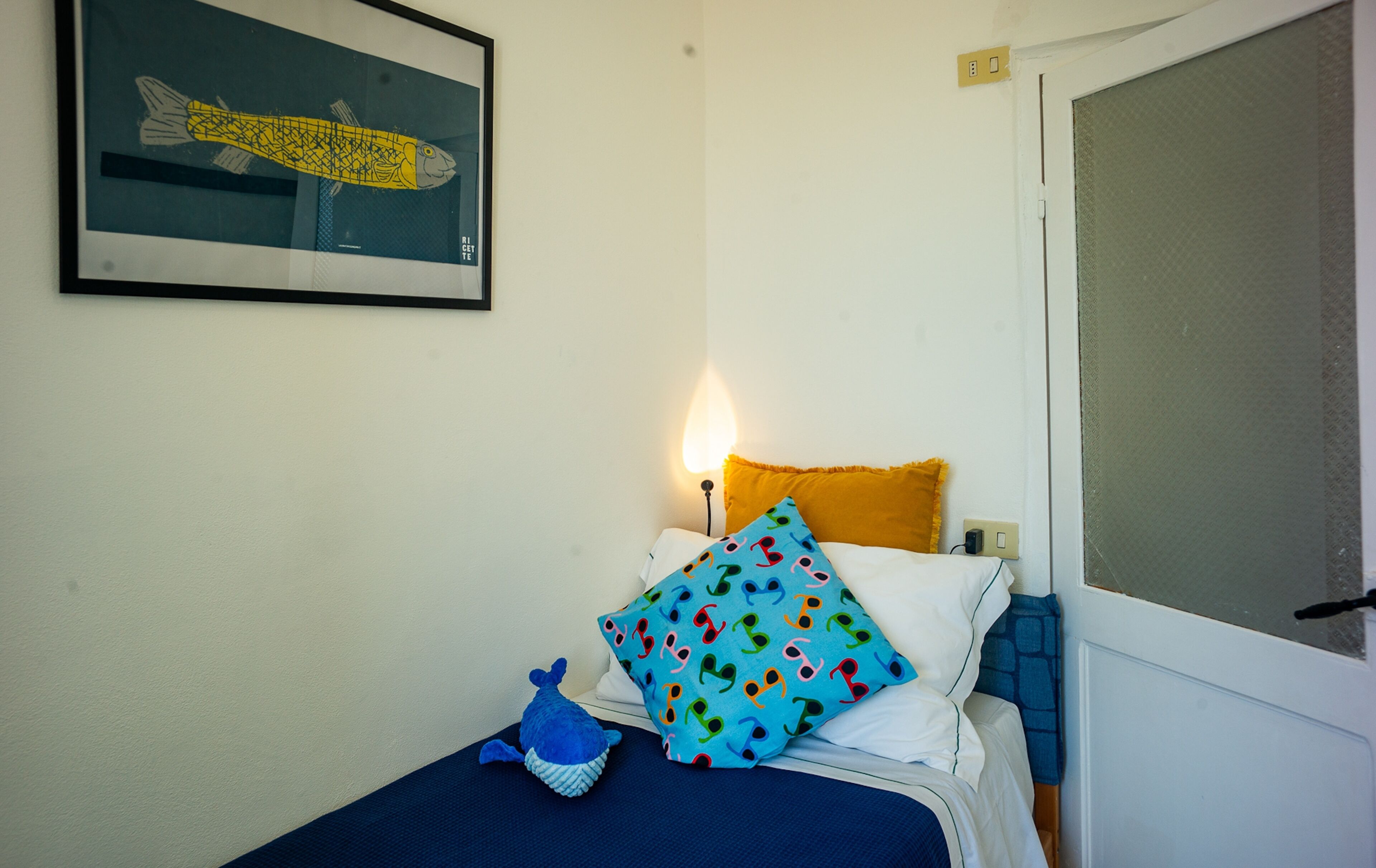 Quarto com cama, quadro na parede, abajur e janela com vista.