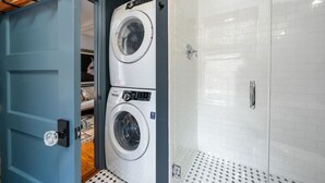 Une buanderie équipée d’un lave-linge et d’un sèche-linge à chargement frontal, d’une porte bleue et d’une zone de douche carrelée.