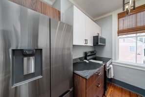 A modern kitchen with stainless steel appliances, wooden cabinets, and a window with blinds.