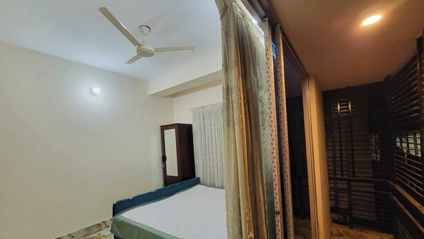 Une chambre à coucher comprenant un lit, un ventilateur de plafond, une armoire et une fenêtre avec des rideaux.