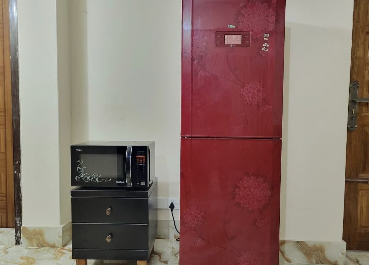 Una cocina compacta con un refrigerador rojo, un microondas y un pequeño electrodoméstico negro sobre un mueble de madera.
