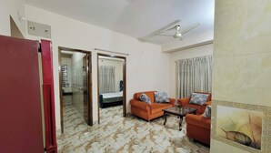Une chambre d’hôtel avec un lit, deux canapés orange, un ventilateur de plafond et un sol à motifs de marbre.