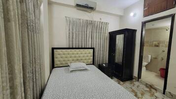 Un dormitorio con cama, armario, aire acondicionado y baño visible a través de una puerta abierta.