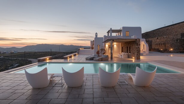 A modern outdoor pool area with white furniture and a stone wall backdrop. - Mykonian Icon Villa (Mykonos)