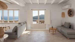 A spacious living room with a large window, a sofa, a coffee table, and a view of the sea. - Mykonian Icon Villa (Mykonos)