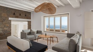A modern living room with a stone wall, a large window with a view, and a hanging wicker light fixture. - Mykonian Icon Villa (Mykonos)