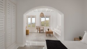 A bedroom with a large window, white walls, and a bed with a black throw. - Mykonian Icon Villa (Mykonos)
