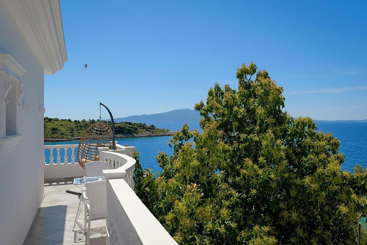 Un balcón con vista al mar, un árbol y un edificio blanco.