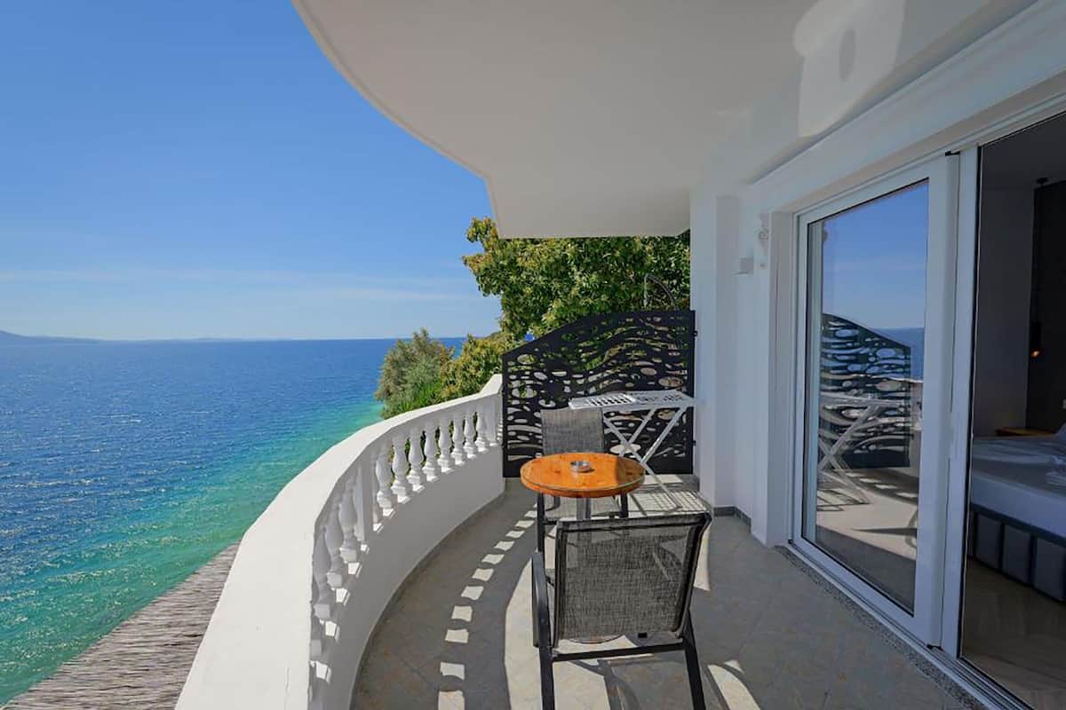 Un balcón con vista al mar, una mesa con una silla y un cristal.