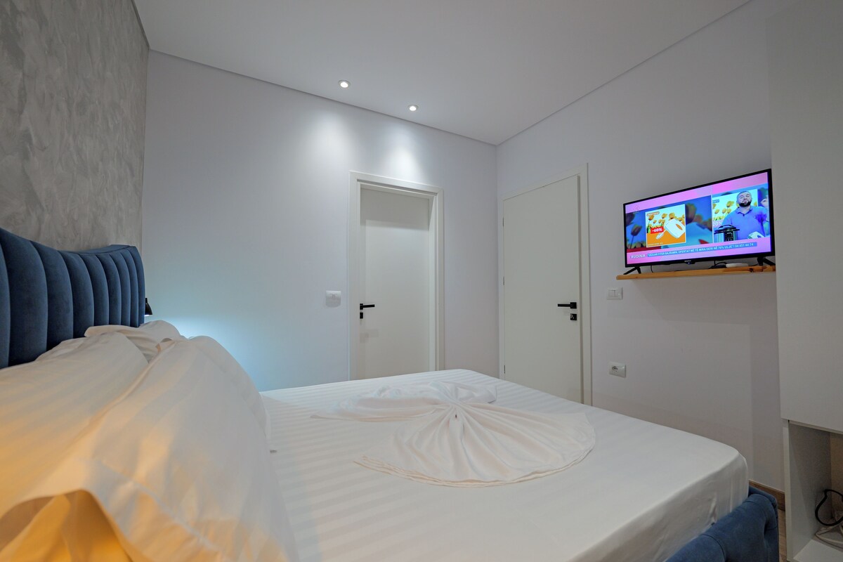 A bedroom with a bed, a television mounted on the wall, and a door leading to another room.