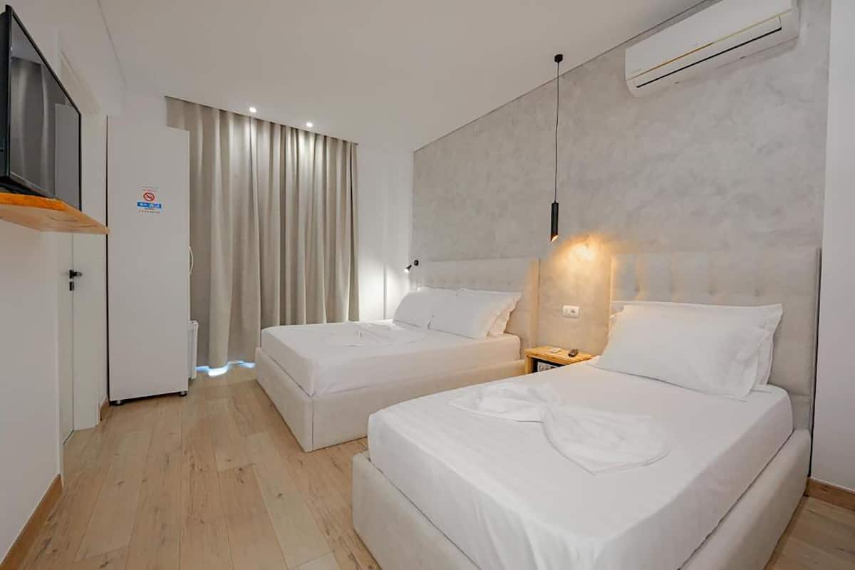 Habitación de hotel moderna con dos camas, televisión, aire acondicionado y vista a la calle.