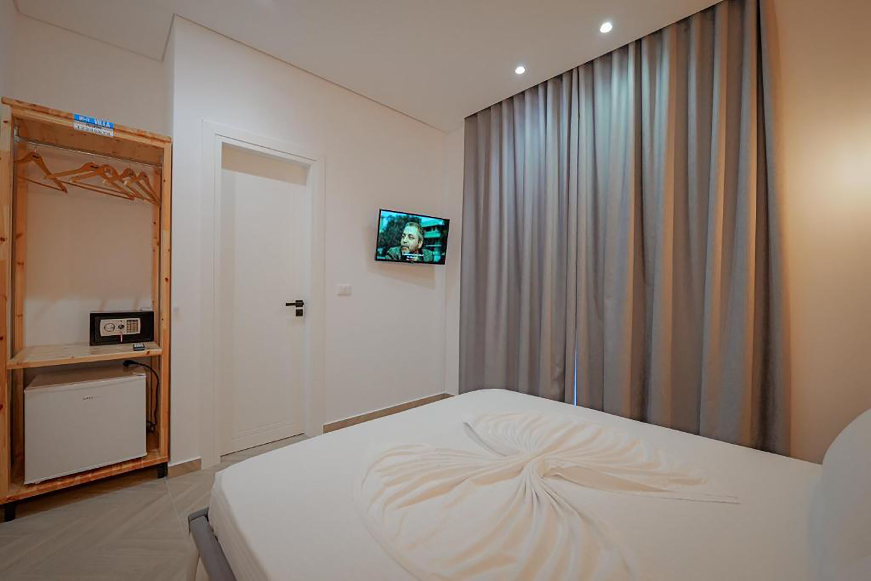 Habitación de hotel con cama, televisor montado en la pared, armario y un refrigerador pequeño.