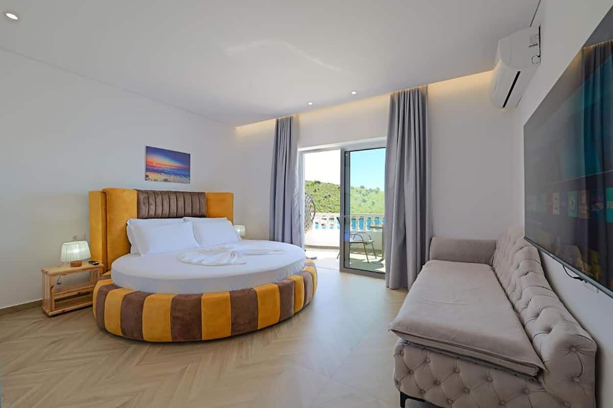 Habitación de hotel moderna con cama redonda, sofá, un cuadro y vistas al exterior.