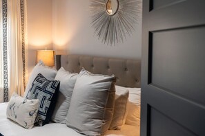 A bedroom with a tufted headboard, a mirror with a sunburst design, and a bed with multiple pillows.