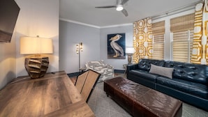 Un salon avec un canapé en cuir foncé, une table basse en bois, un tapis à motifs, un ventilateur de plafond et une lampe fixée au mur.