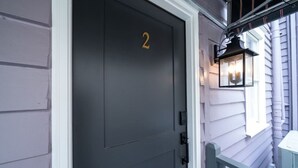 Une porte gris foncé portant le numéro 2, un chambranle blanc et une lanterne noire sur le côté droit.