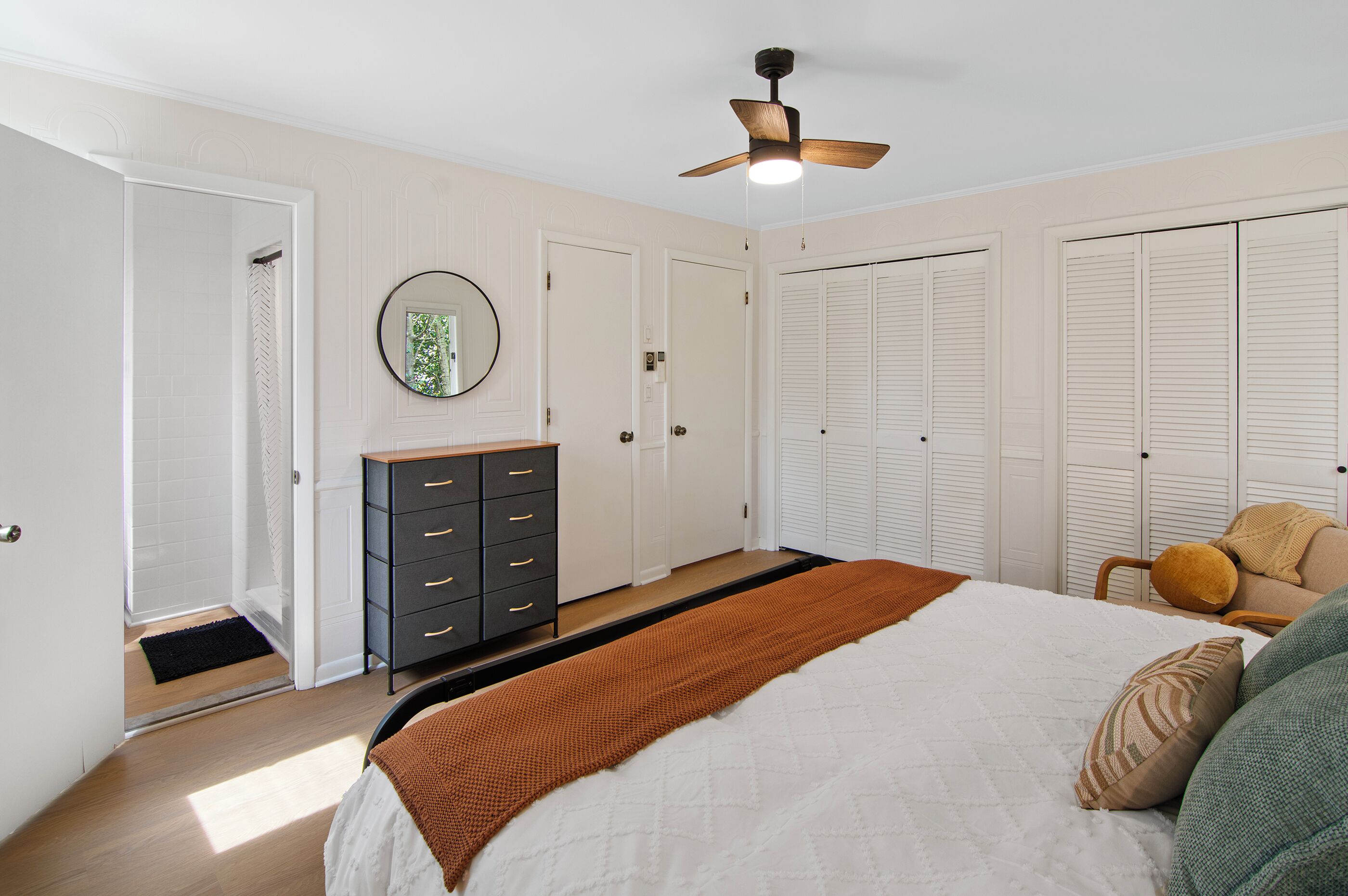 A bedroom with a bed, a dresser, a ceiling fan, and a closet.
