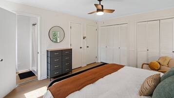 A bedroom with a bed, a dresser, a ceiling fan, and a closet.