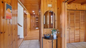 Un pasillo de madera con una escalera, un espejo y una pequeña mesa con un cuenco y flores.