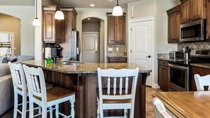 A kitchen with a central island, white chairs, wooden cabinets, and stainless steel appliances. - House w/private pool & free access to Sand Hollow (Hurricane)