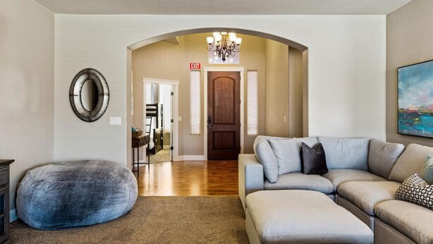 A living room with a sectional sofa, a round ottoman, a chandelier, and a painting on the wall. - House w/private pool & free access to Sand Hollow (Hurricane)