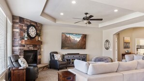 A living room with a fireplace, a ceiling fan, a large painting, and a sofa. - House w/private pool & free access to Sand Hollow (Hurricane)