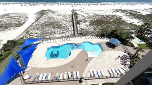 A beachside resort with a swimming pool, sun loungers, and a view of the ocean.
