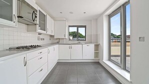 A modern kitchen with white cabinets, a gas stove, and a window providing a view of the outside. - Luxurious 3 Bedroom Penthouse in City Centre (Chelmsford)
