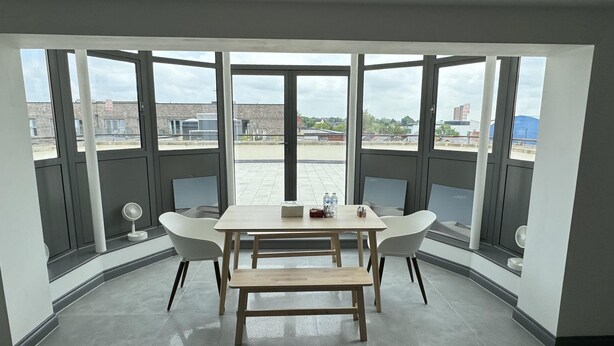 A corner room with a large window, a wooden table, two white chairs, and a bench. - Luxurious 3 Bedroom Penthouse in City Centre (Chelmsford)