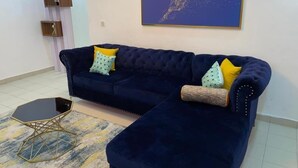 A dark blue sofa with yellow and patterned cushions, a gold-framed side table, and a blue abstract painting on the wall.