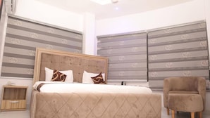 A bedroom with a large bed, a nightstand, a chair, and patterned curtains.