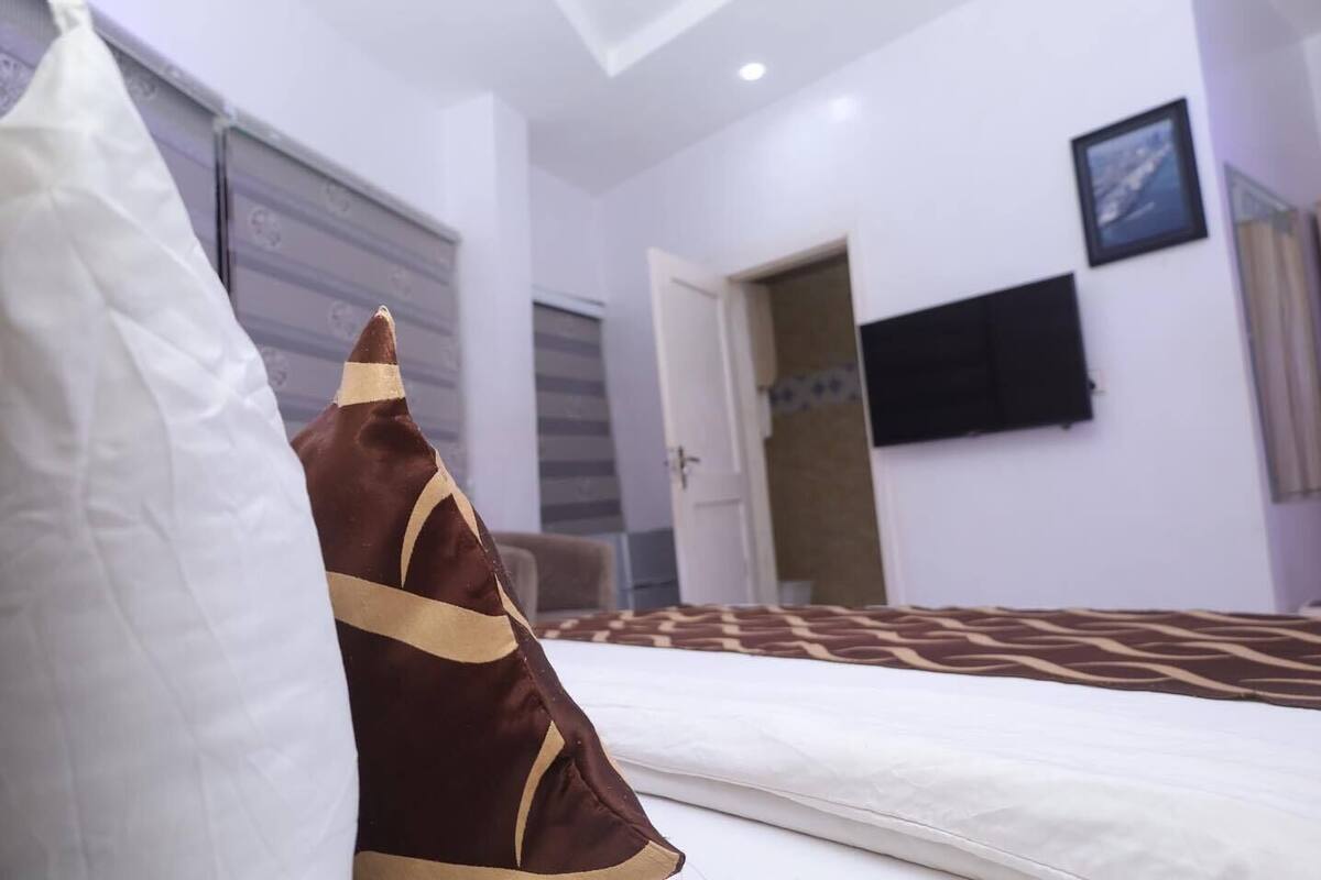 A hotel room with a bed, a door, and a wall-mounted TV.