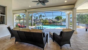 A covered outdoor area with wicker furniture, a ceiling fan, and a view of a swimming pool and palm trees. - Elegant 4-BR Tempur Pedic w/ Pvt Pool & Beach Access (Cape Coral)